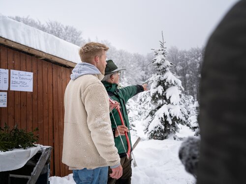 Zwei Personen stehen im Schnee neben einer Hütte.